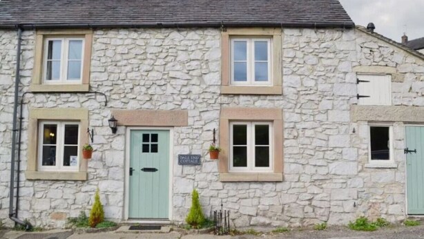 Een stenen cottage met een groene deur, twee ramen en een bordje met de tekst 'Dale End Cottage'.