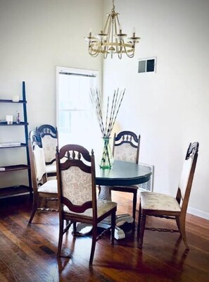 A dining area with a round table and four chairs, a chandelier, and a shelving unit.