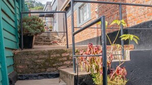 Un étroit escalier extérieur mène à un bâtiment en briques, doté d’une rambarde en métal et de plantes en pot.