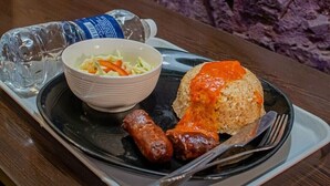 Un repas composé de riz, de saucisses et d’une salade, le tout servi dans une assiette noire.