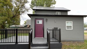 Un bâtiment à deux étages avec une porte rouge, une petite fenêtre et une rambarde noire menant à l’entrée.