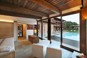A modern interior with a large glass door leading to a pool area, wooden ceiling beams, and a cozy seating area with a table and chairs. - Agriturismo Malabaila (Canale)