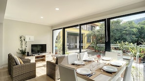 A modern dining area with a large window, wicker furniture, and a flat-screen TV. - Solarium Villa by Atlantic Holiday (Machico)