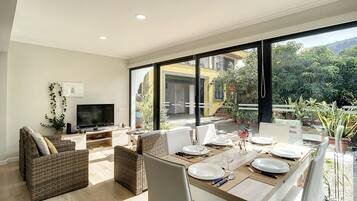 A modern dining area with a large window, wicker furniture, and a flat-screen TV.
