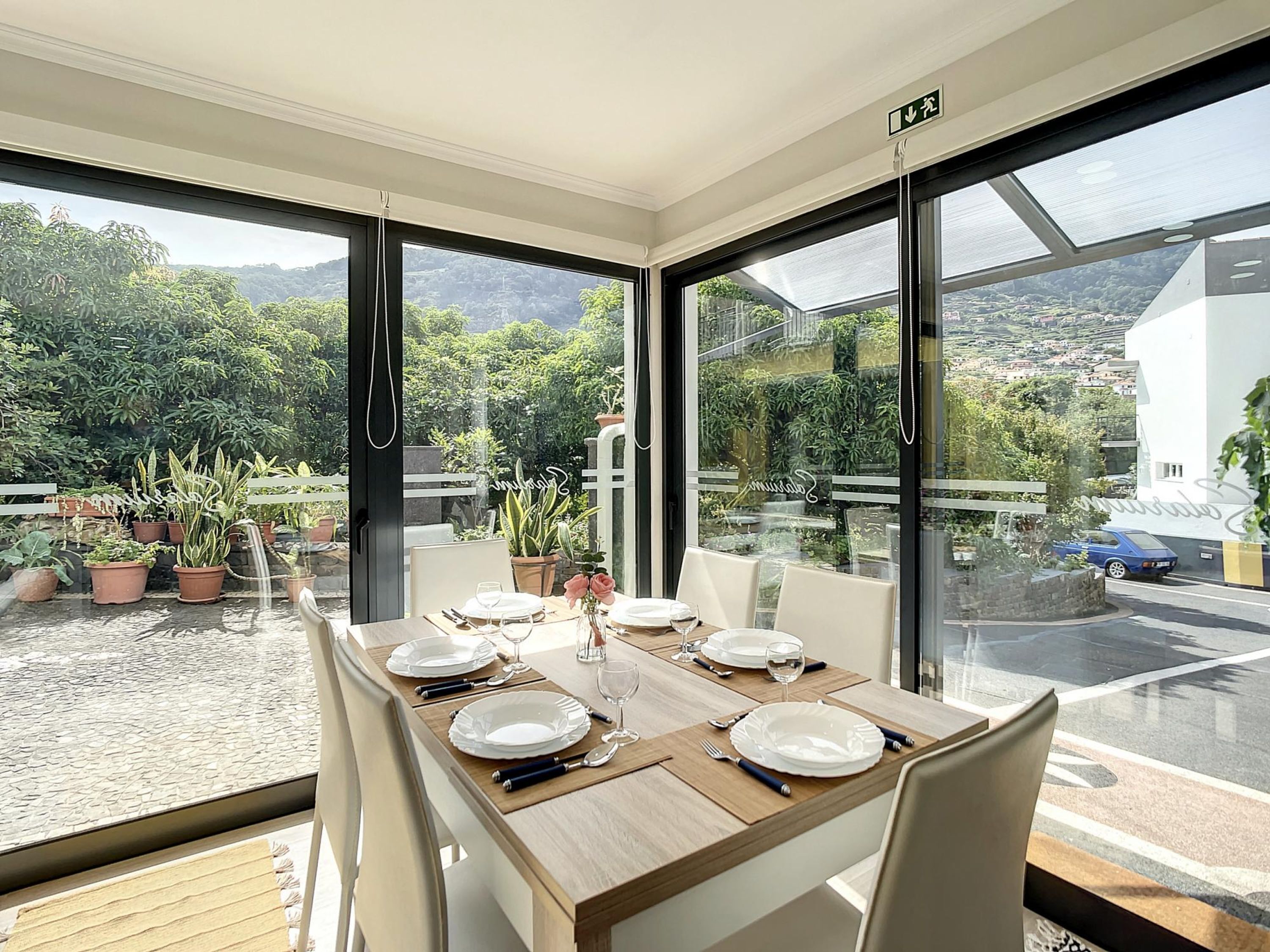 A dining area with a table set for four, large windows, and potted plants.