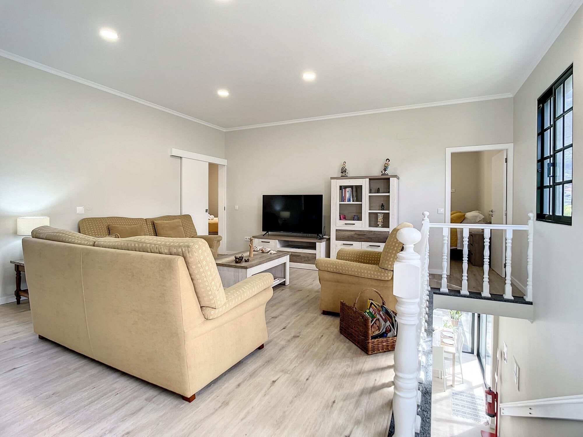 A spacious living room with a beige sofa, a coffee table, a TV, and a bookshelf.