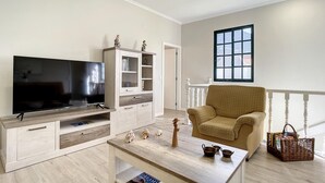 A living room with a flat-screen TV, a wooden cabinet, a beige armchair, and a coffee table with decorative items. - Solarium Villa by Atlantic Holiday (Machico)