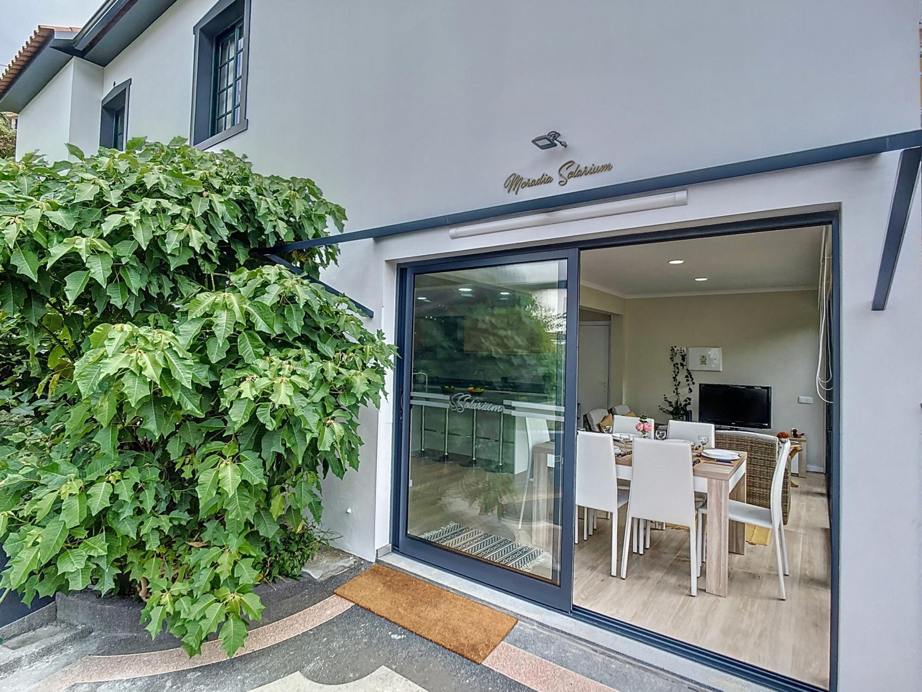 A modern building with a glass door leading to an interior dining area with white furniture.
