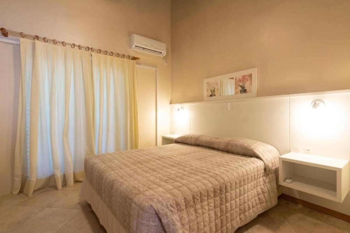Une chambre à coucher comprenant un lit, des rideaux, un appareil de climatisation, une table de chevet et une étagère fixée au mur.