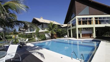 Piscina com espreguiçadeiras e um edifício de dois andares com grandes janelas.