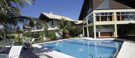 Una piscina con sillones de descanso y un edificio de dos pisos con ventanas amplias.