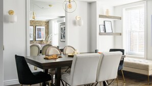 Zona pranzo con tavolo in legno scuro, sedie bianche e lampada a sospensione moderna.