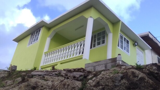 Una casa de dos pisos amb un balcó, una base de pedra i un cel serè.