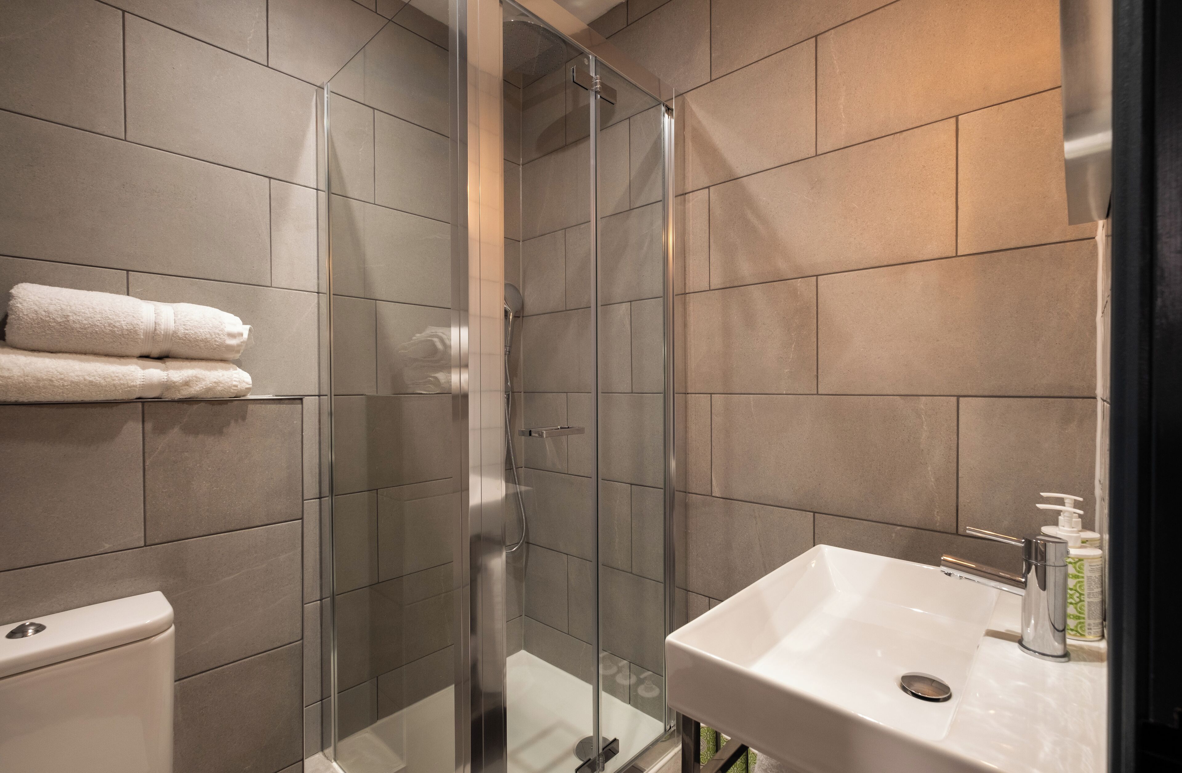 Un baño moderno con ducha de vidrio, lavamanos blanco y retrete.