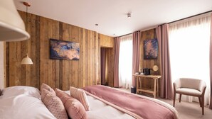 A hotel room with a wooden wall, a bed with pink bedding, a desk with a chair, and artwork on the wall. - The Stroud Hotel (Stroud)