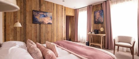 A hotel room with a wooden wall, a bed with pink bedding, a desk with a chair, and artwork on the wall.