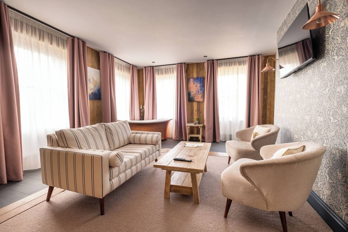 A living room with a sofa, armchair, and coffee table, a small side table, and a TV mounted on the wall.