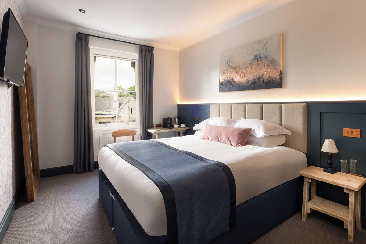 A hotel room with a large bed, bedside tables, a TV, and a window with curtains.