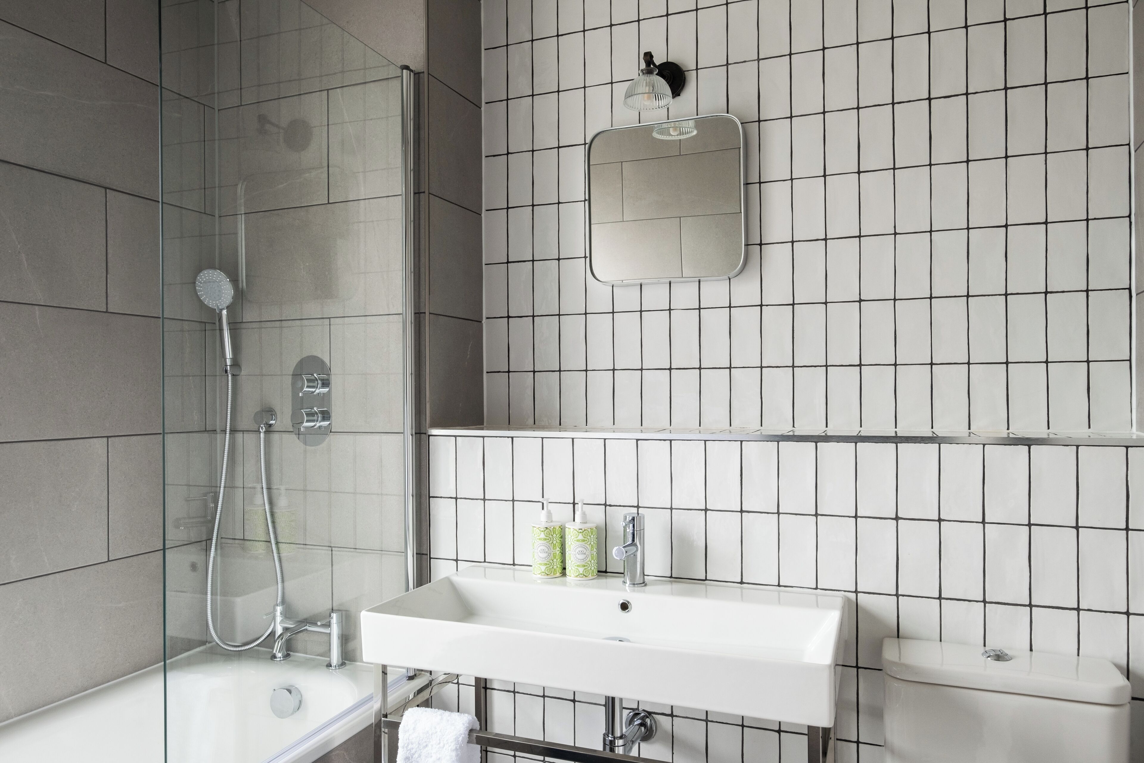 Un baño con cabina de ducha de vidrio, un lavamanos blanco, un inodoro y un espejo en la pared.