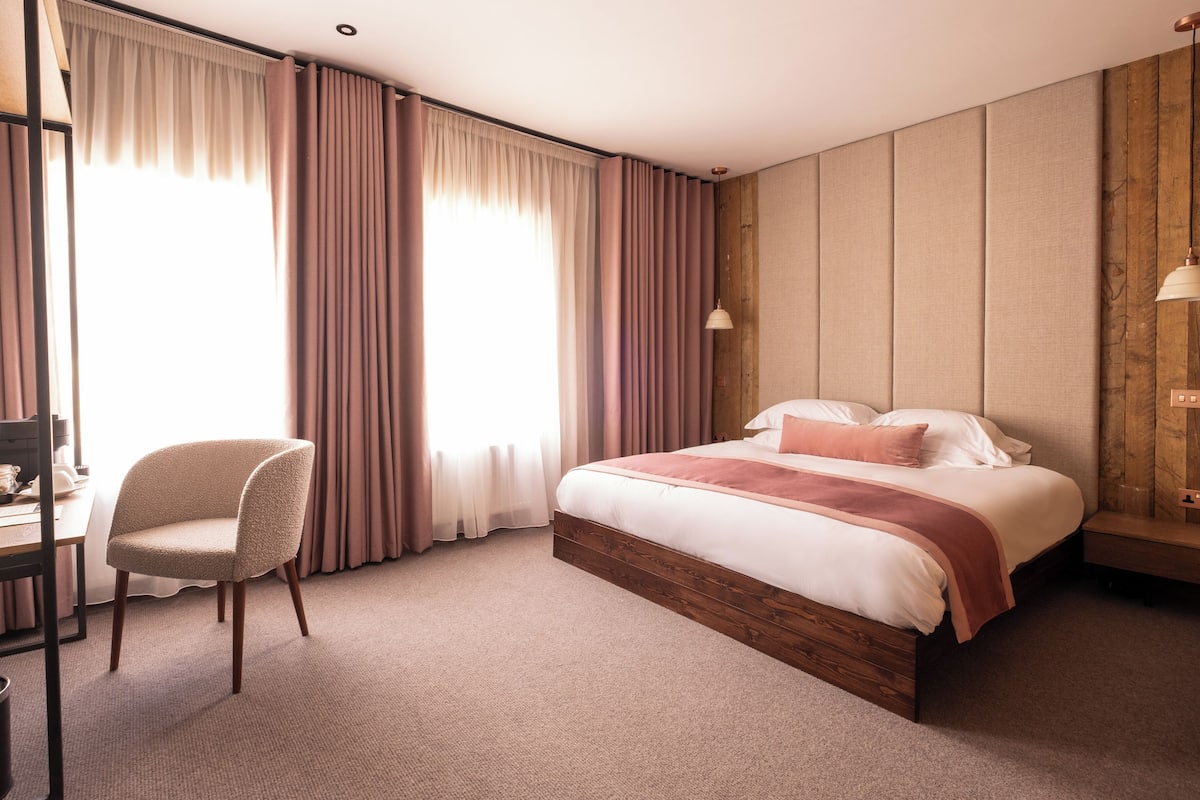 A hotel room with a bed, a chair, a desk, and a wooden wall panel.