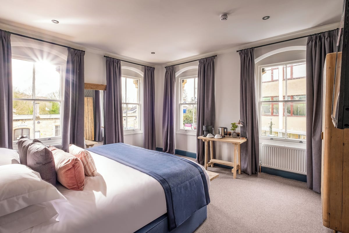 A hotel room with a large bed, a desk, and two windows with curtains.