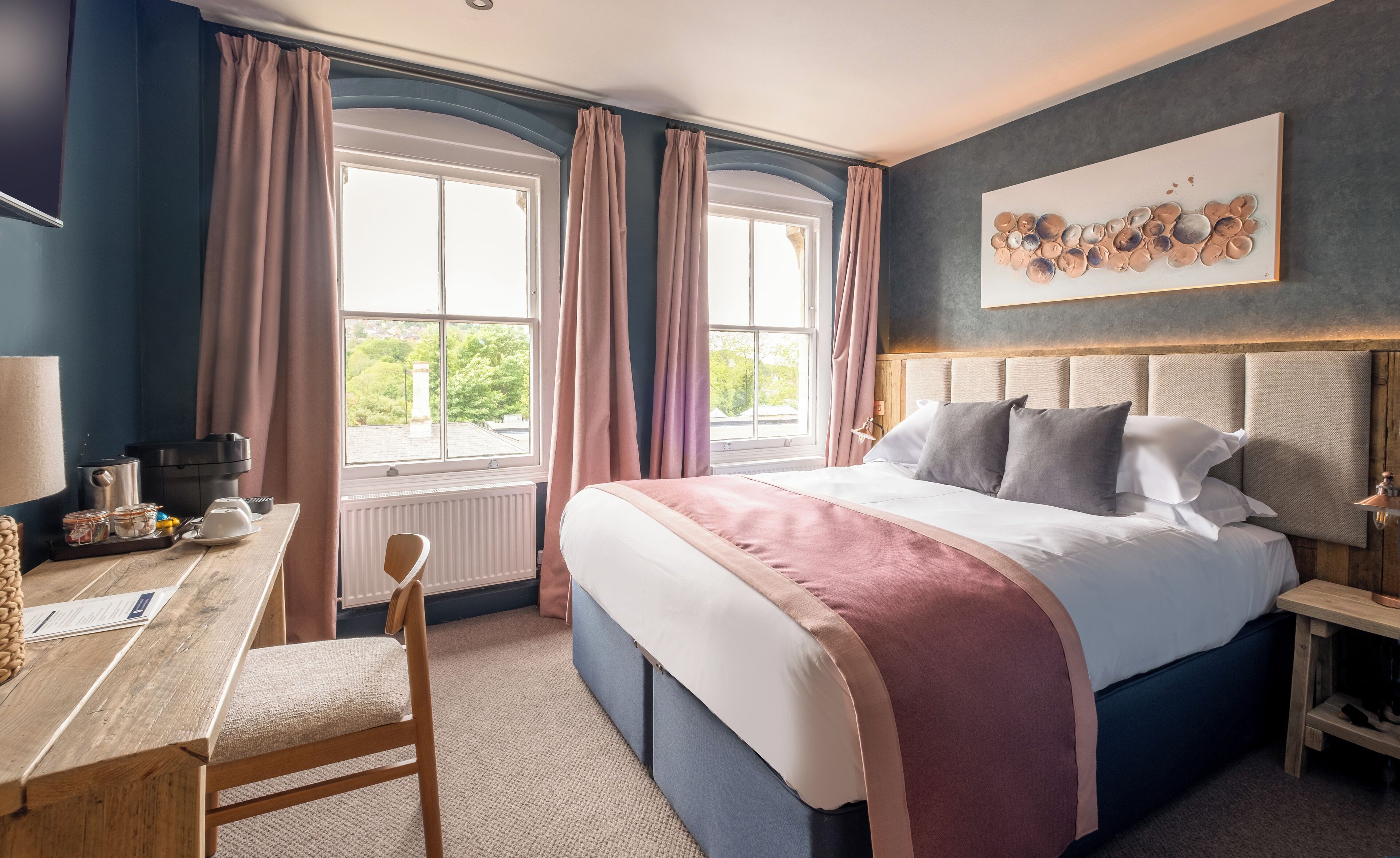 A bedroom with a bed, a desk, and a window with curtains.
