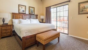A bedroom with a large bed, wooden headboard, two bedside tables with lamps, a bench, and a view of the outdoors through a large window. - 1Bed/1Bath - Gorgeous Flagstaff Location with Pools, Golf, and More! (Flagstaff)