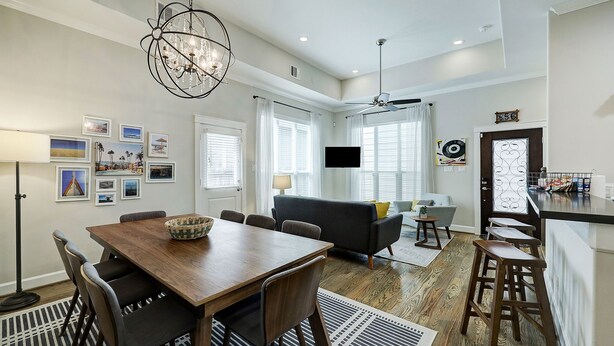 A modern living room with a wooden dining table, dark sofas, and a chandelier.