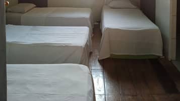 Una habitación con dos camas individuales, una ventana con cortinas, un equipo de aire acondicionado y piso de madera.