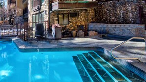 Une piscine avec un mur en pierre et des chaises longues.