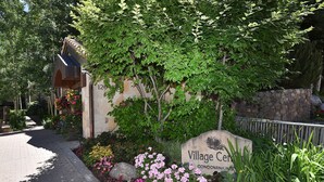 Une enseigne pour le complexe d’appartements « Village Center », avec un chemin en briques et des plantes en fleurs.