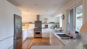 Una cocina moderna con armarios blancos, un refrigerador de acero inoxidable, una estufa a gas y un amplio ventanal que proporciona luz natural.