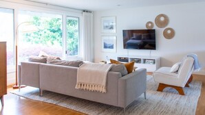 Una sala de estar moderna con un sofá gris, un sillón blanco y un televisor en la pared.