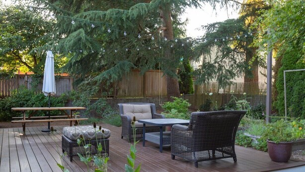 Una terraza de madera con mobiliario exterior, que incluye una mesa y sillas, rodeada de vegetación y una valla de madera.