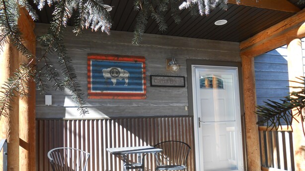 Eine Holzfassade mit einem rustikalen Metallschild, einer Tür und zwei Metallstühlen.