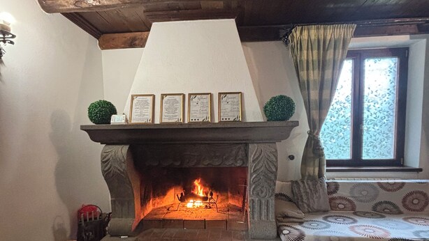 Una habitación acogedora con chimenea, sillones de mimbre con girasoles, una alfombra estampada y una ventana con cortinas.