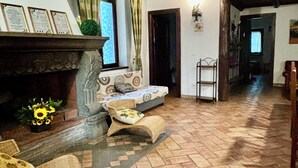 Una sala de estar acogedora con chimenea, un sofá y un sillón. El suelo es de madera y hay una escalera que lleva a otra habitación.