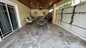 A covered patio area with stone flooring, a dining table with chairs, and a ceiling fan. - GuestHome 5 minutes from Miami Airport with Heated Pool  (Miami)