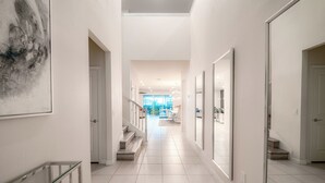 Ein moderner Flur mit Glastrennwand, weißen Wänden und einer Treppe zu einem hellen Raum mit großen Fenstern.