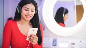 Una persona con suéter rojo sosteniendo un teléfono inteligente frente a un espejo con un aro de luz.