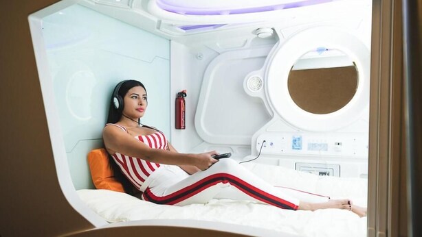 Una habitación médica futurista con un paciente acostado en una cama, un panel de control y un ventanal circular.