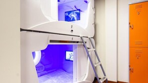 Una cama litera con televisor en la parte superior, una escalera y un armario para guardar objetos en la habitación.
