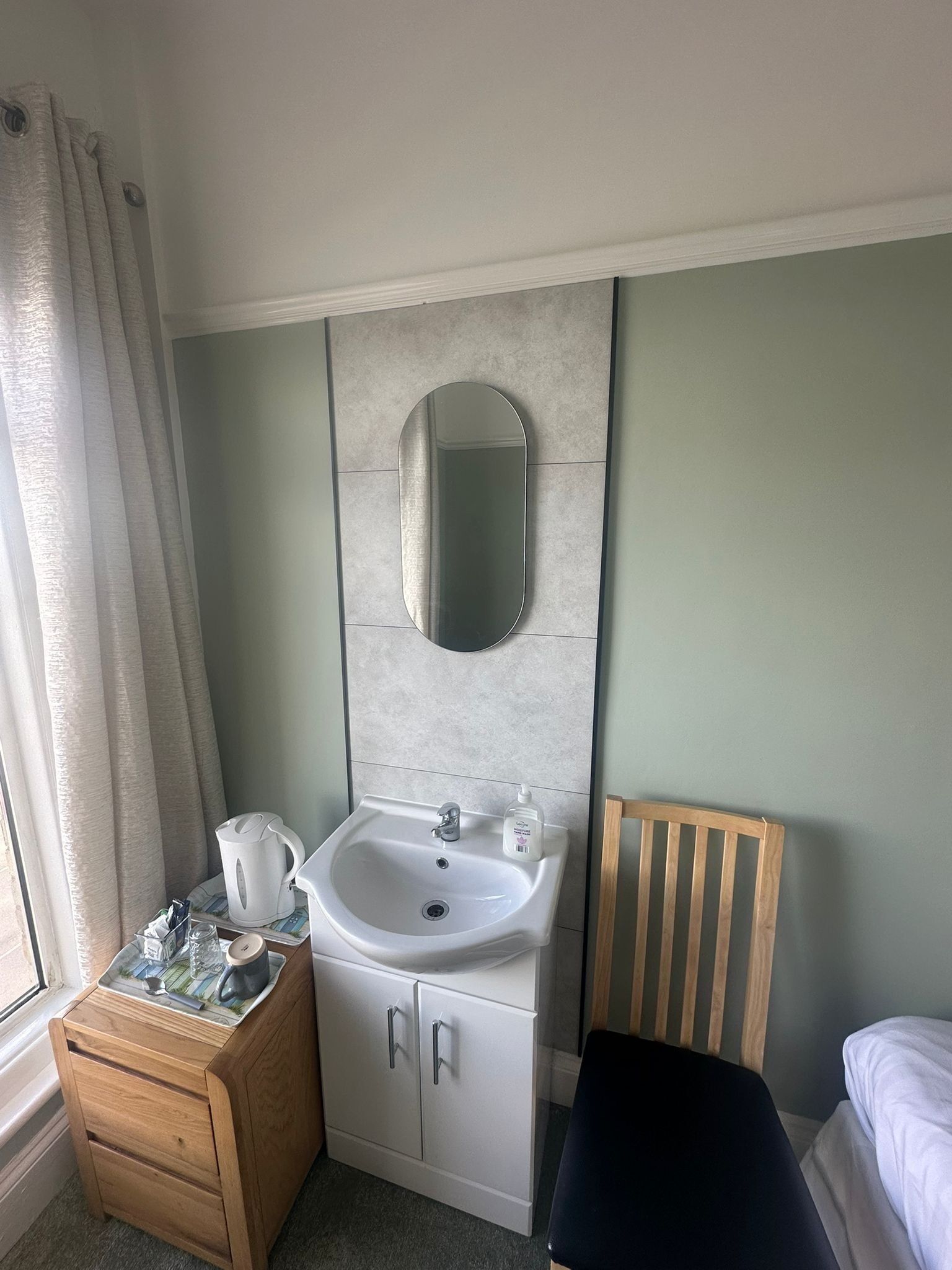 A bathroom with a sink, mirror, wooden cabinet, and a chair.