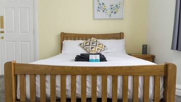 A wooden bed with a white mattress, a geometric pillow, and a folded towel.