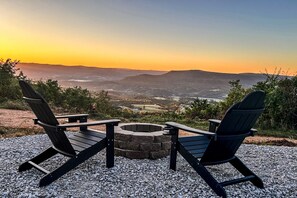 To Adirondack-stole vender mod en ildsted i sten med udsigt over en dal og bjerge i solnedgangen.