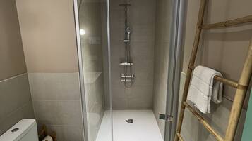 Un baño moderno con ducha envuelta en vidrio, inodoro y toallero de bambú.