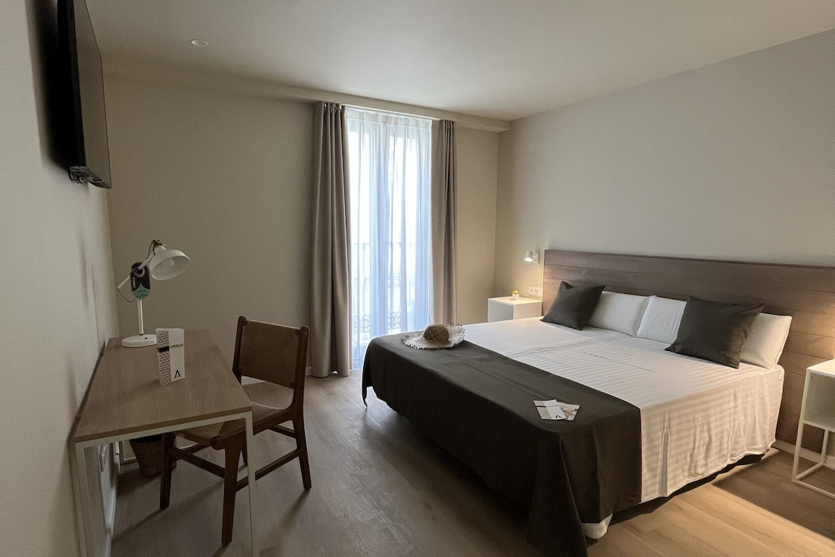A hotel room with a bed, a desk, a chair, a TV, and a window with curtains.