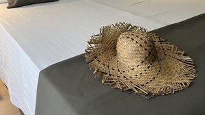 Una cama bien hecha con sábanas blancas y un edredón gris oscuro, un cabecero de madera y una mesita de noche con una lámpara y una pequeña planta en maceta.