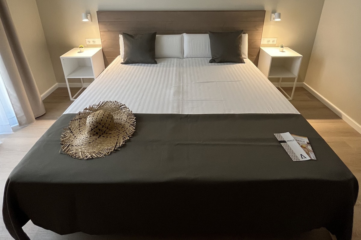 A hotel room with a large bed, two bedside tables, a headboard, and a floor lamp.