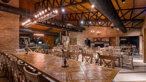 A spacious dining area with a large wooden table and chairs, a stone wall, and a modern kitchen in the background. - Giuaani Winery (Sagarejo)